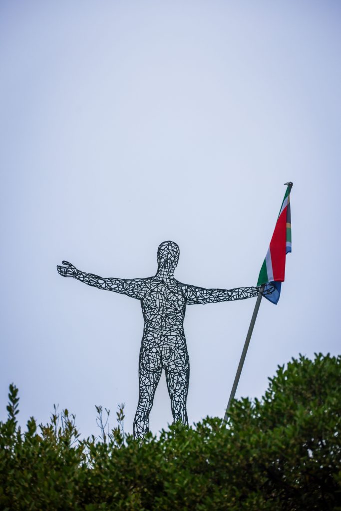Artistic wire sculpture holding the South African flag against a clear sky.