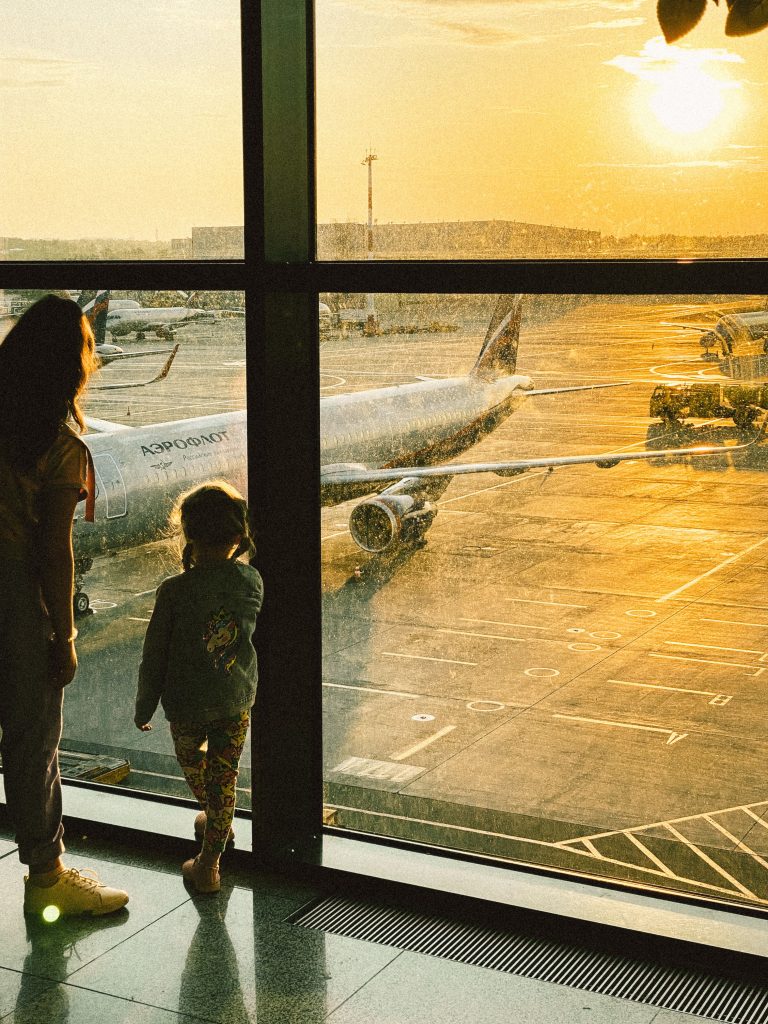 A mother and daughter watch planes at Moscow airport during sunrise. Travel concept.